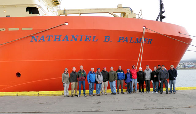 Group of people stands in front of ship.