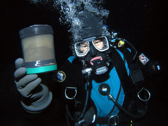 Diver holds container under water.