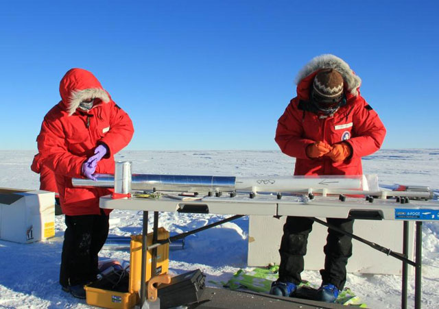 Two people handle an ice core on a table.