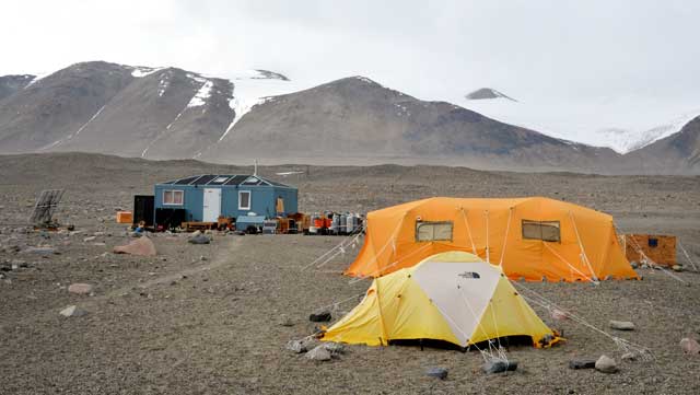 Tents and small buildings sit in front of barren mountain.