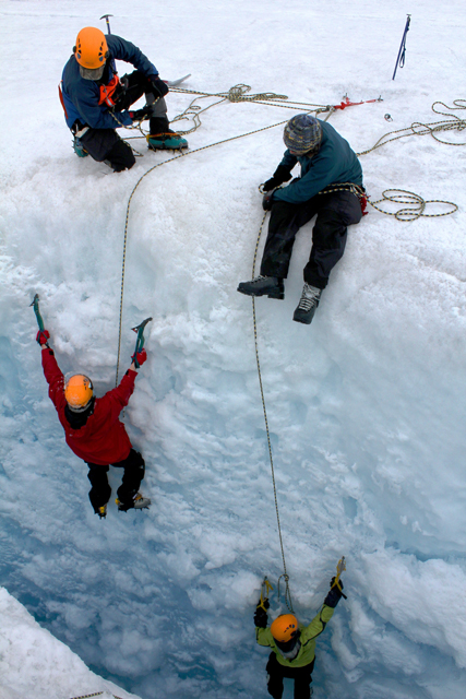 People belay others down a crevasse.