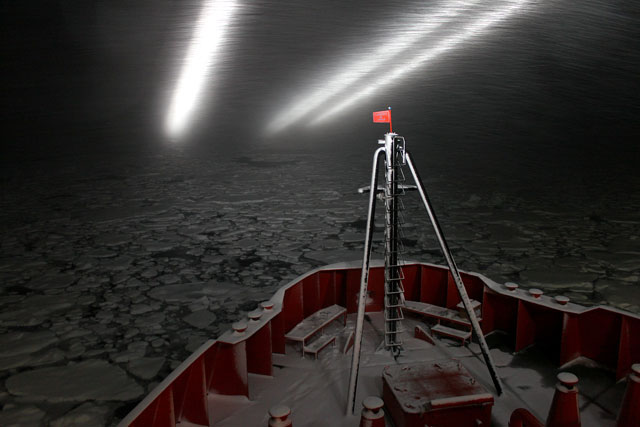 A ship pushes through ice at night.