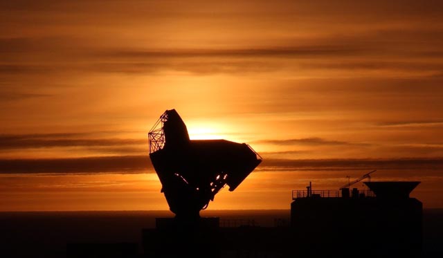 Telescope backlit by setting sun.