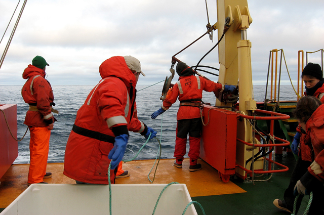 People on deck of ship pull rope.