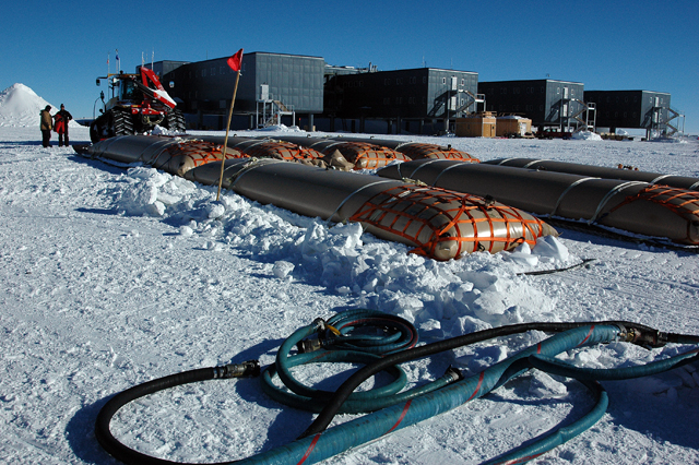 Fuel bladders on sled in front of large building.