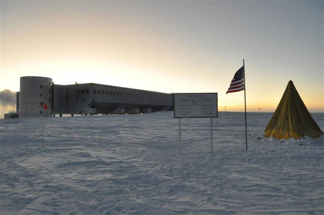 Large building on snow with tent, sign and flag in foreground.