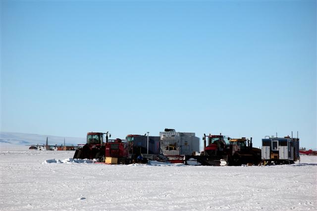 Tractors and buildings on ice with planes in background.