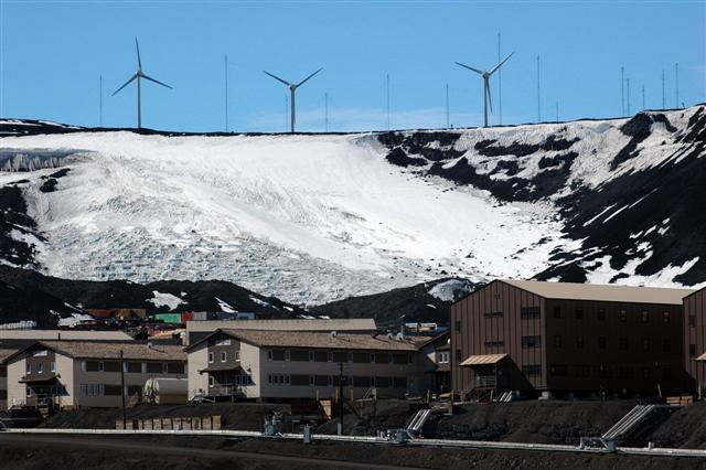 Windmills behind buildings and a hill.