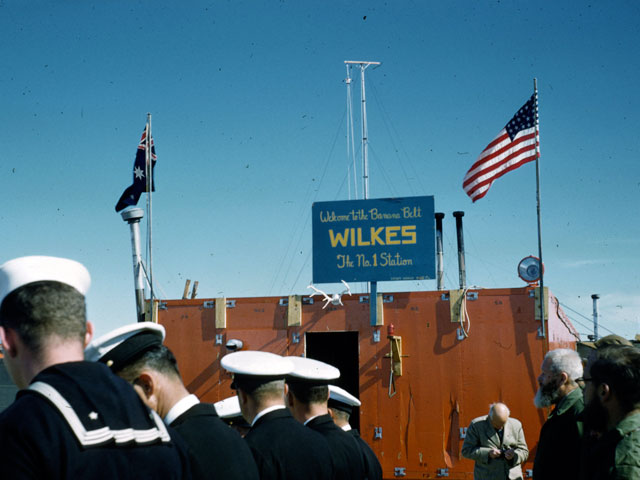 Men in naval uniforms stand near a building.