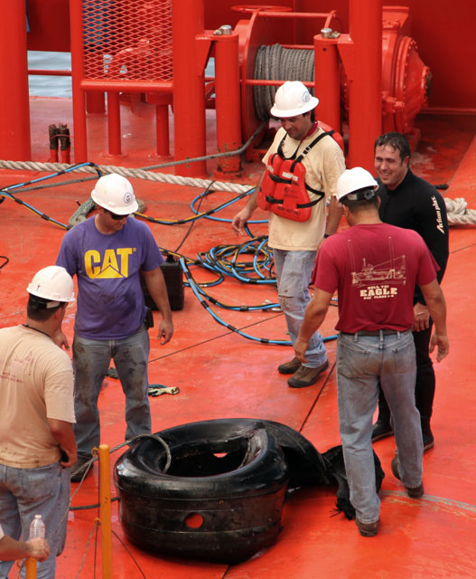 People surround tire on ship deck.