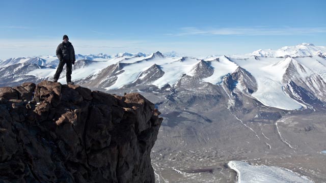 Person stands on peak in mountain range.