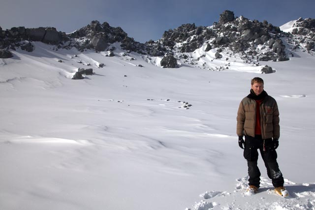Person stands in snowy, rocky landscape.