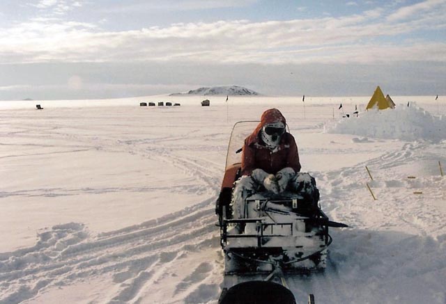 Person sits on snowmobile in snowy place.