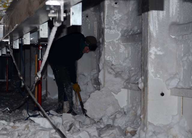 Person shovels ice from underneath a building.