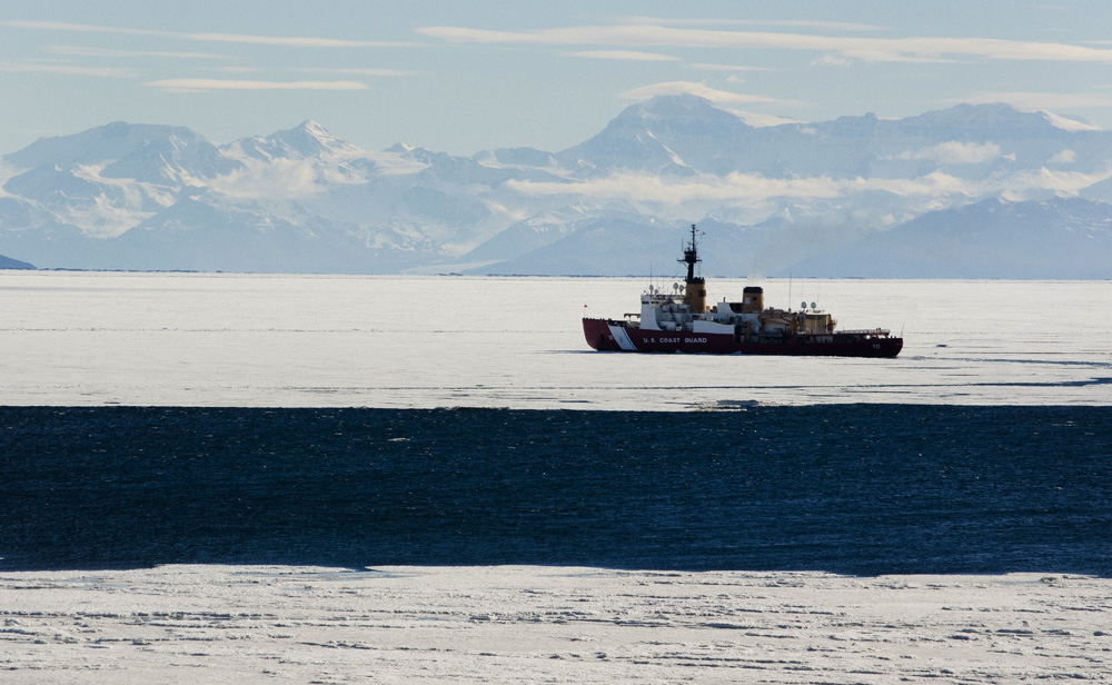 Ship sails in ocean between ice floes.