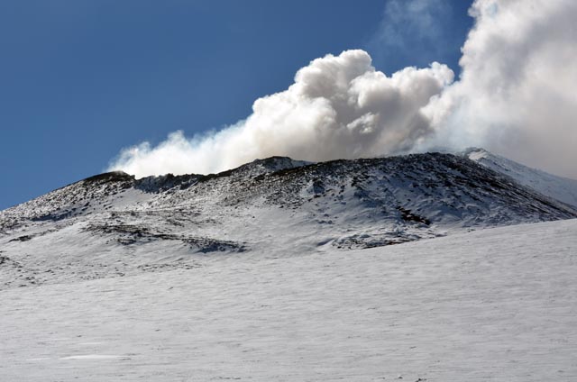 Smoke emerges from cone of volcano.