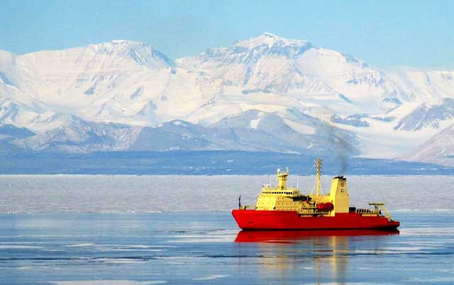 A ship in calm water in front of glaciated mountains.