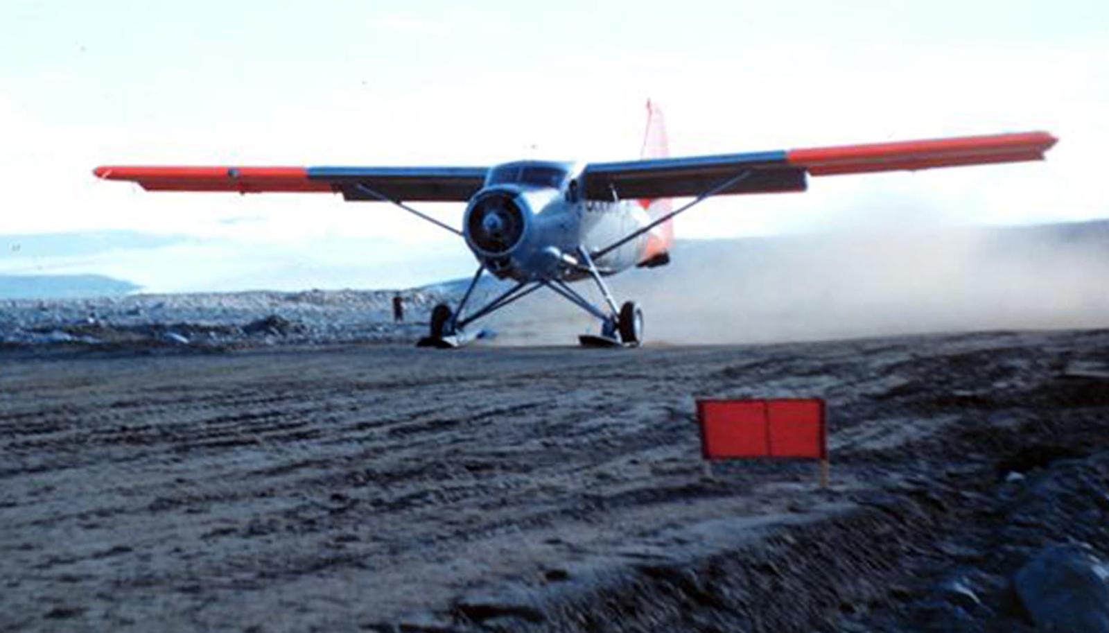 Old-style plane lands on dirt runway.