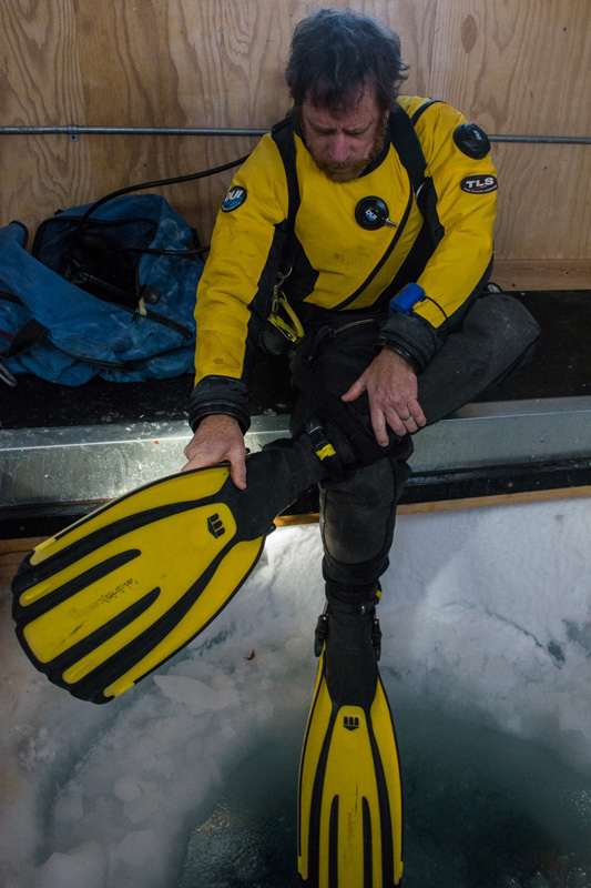 Perched above a hole in the sea ice, Robbins dons his fins before a dive.