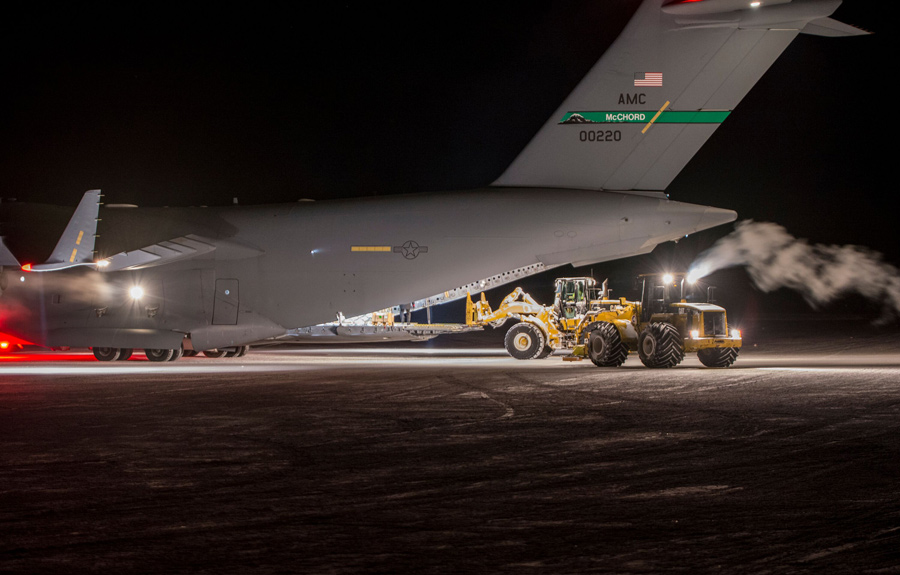 A forklift unloads cargo off of an Air Force C-17 in the July darkness