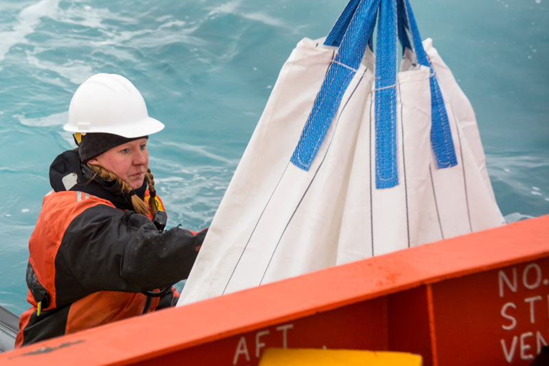 Marine technician Amy Belcher guides a load of supplies onto a small Zodiac raft