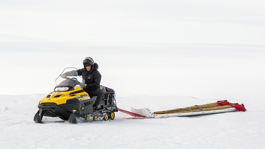 Field safety coordinator Philippe Wheelock drives a snowmobile across the ice shelf. Using the flags in tow, he's helping to mark the safe travel routes across the frozen landscape.