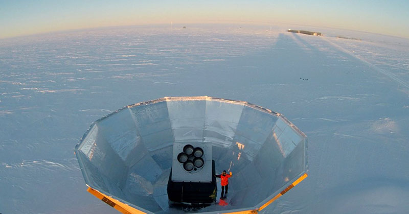 The five receivers of the Keck Array are shielded from blowing snow by its surrounding ground shield. The elevated station in the background is about half a mile away