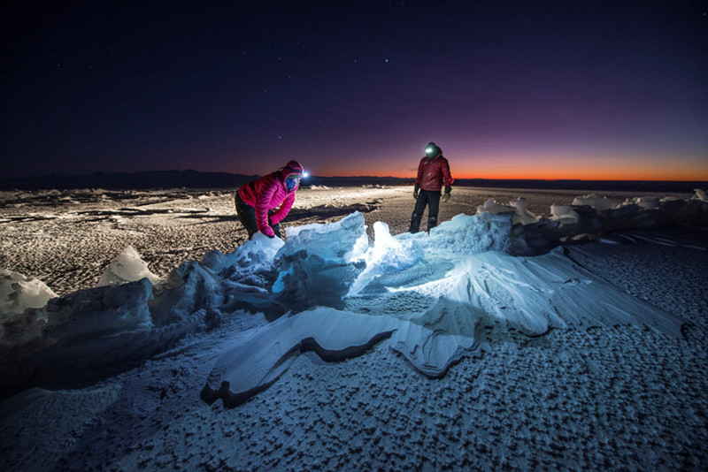 In the Antarctic twilight, two members of the sea ice team inspect a crack in the sea ice