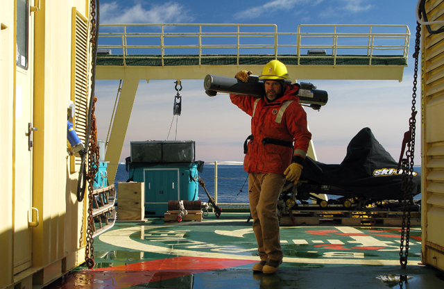 Man carries instrument on ship deck.