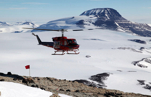Helicopter flies near snow-covered mountains.