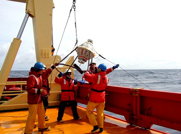 Scientists and ship crew deploy an oceanographic instrument.