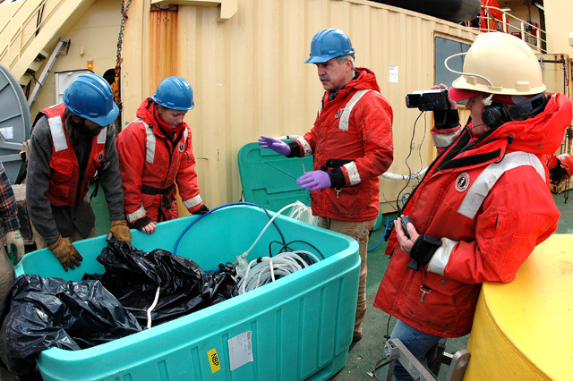 Scientists and ship crew peer into a box.
