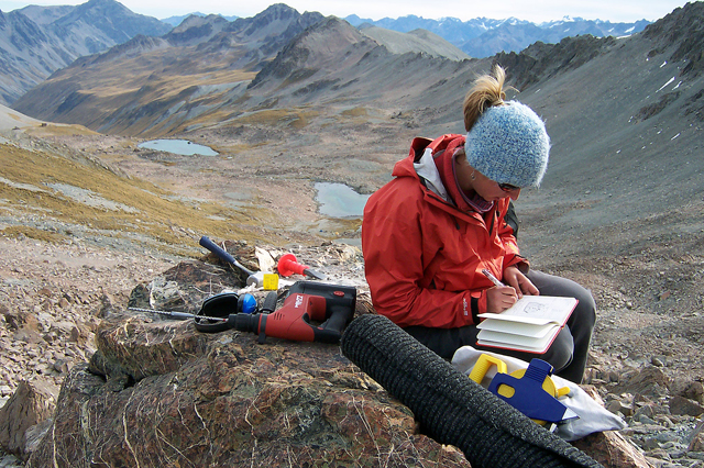 Woman sits on rock taking notes.