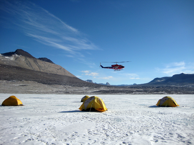 Helicopter flies over tents.