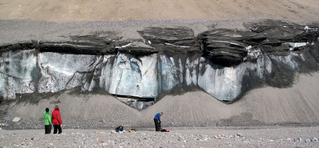 People stand next to cliff of sediment and snow.