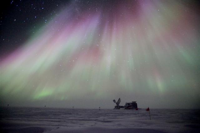 An aurora shimmers above a building on a plateau.