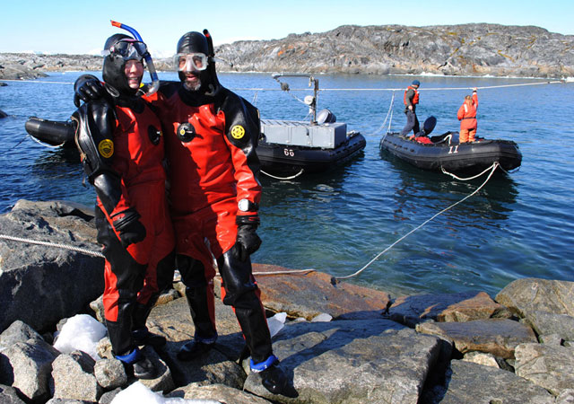 Two divers stand in front of water.