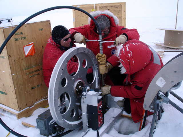 People work with instrument in snowy conditions.