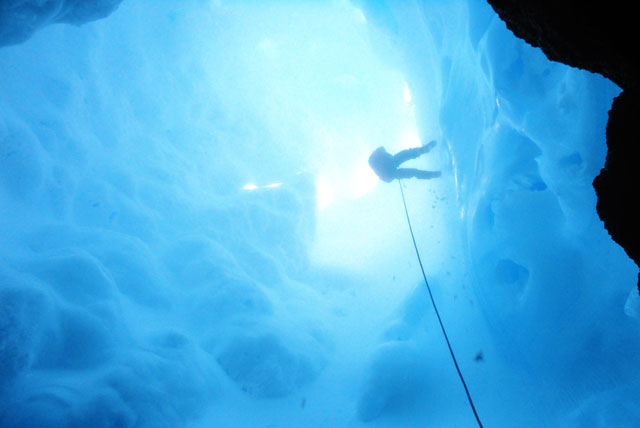 Person climbs down rope into ice cave.
