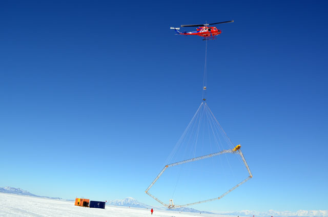 Helicopter carries instrument over ice.