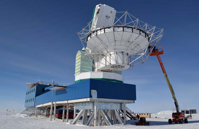 Workers assemble metal girder around telescope.