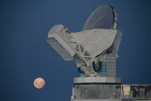 Full moon shines behind telescope.