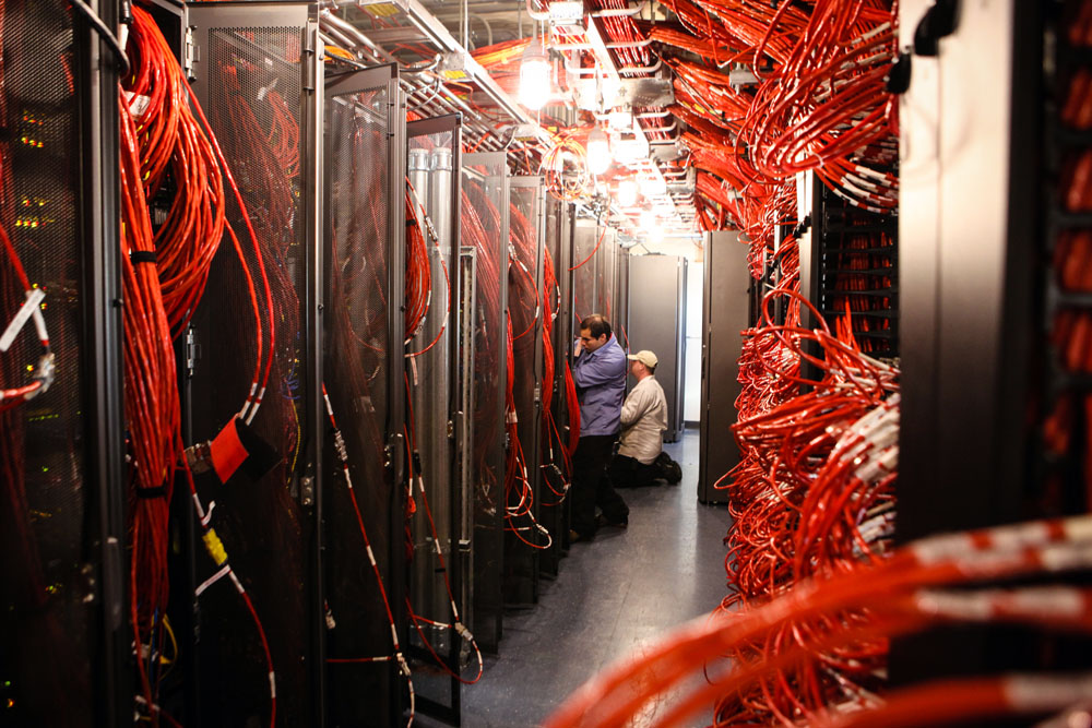 People work in a computer server room with lots of cables.