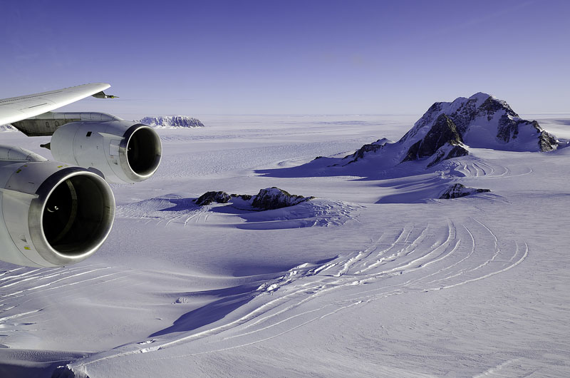 A plane wing is visible of plane flying over icy landscape.