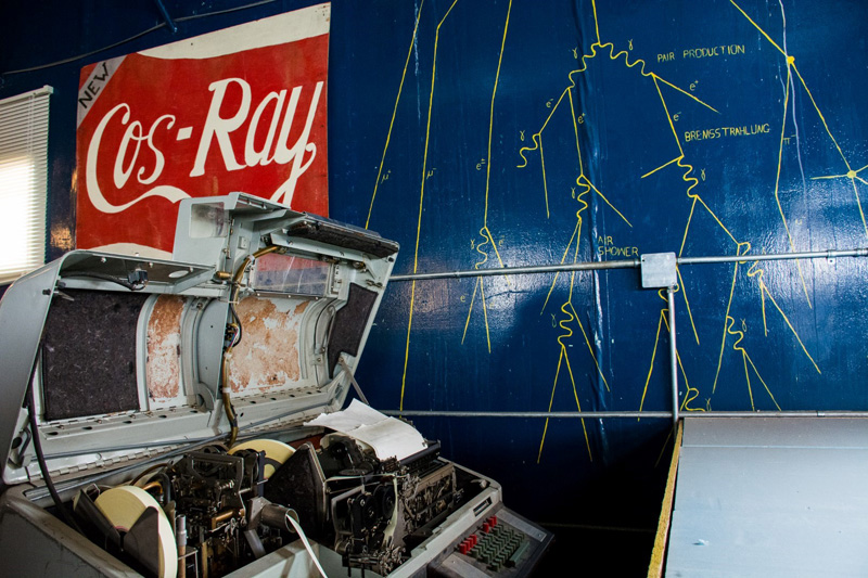 A mural depicting an air shower from a cosmic ray adorns the wall behind an old ticker tape readout unit next to the CosRay detectors.