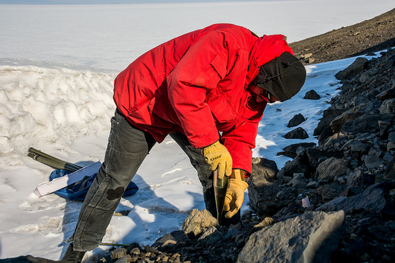 On the side of Observation Hill at McMurdo Station, Alex Chartier installs an anchor into the ground to help secure one of his instruments.