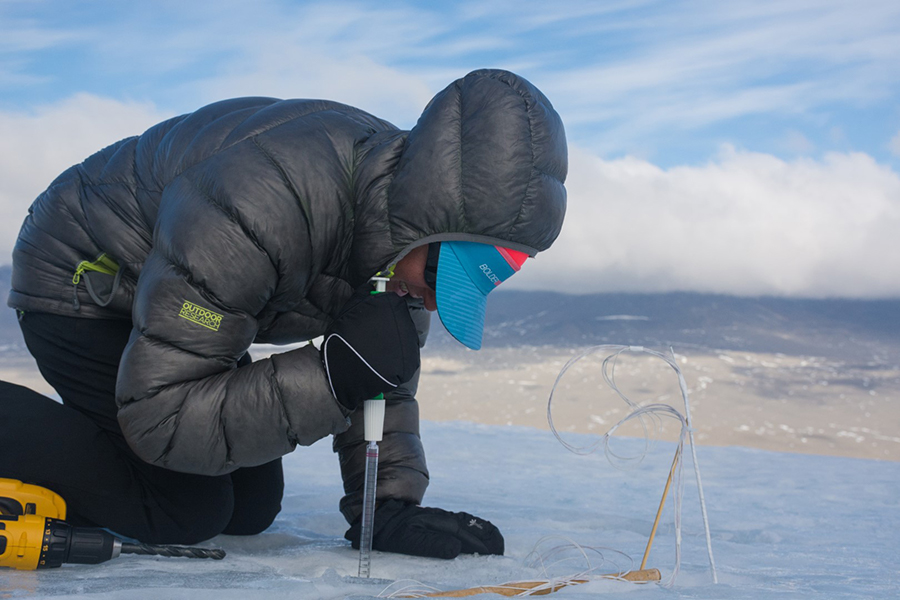 Dorota Porazinska uses a large pipette to sample the liquid water frozen inside of a drilled out cryoconite hole