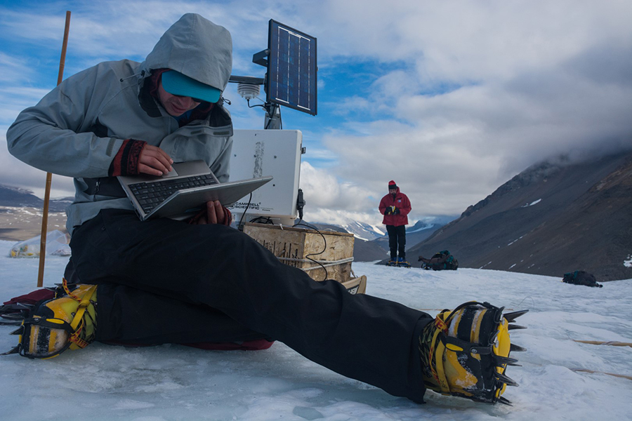 Jack Darcy (foreground) downloads climate data off of a monitoring station that records the weather conditions adjacent to the cryoconite holes as Andrew Fountain looks on