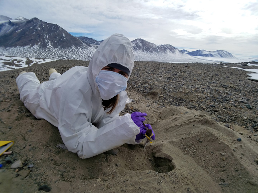 While wearing a sterile over suit to prevent contamination, Sarah Johnson collects samples of desiccated microbial from an ancient lake bed in Taylor Valley.