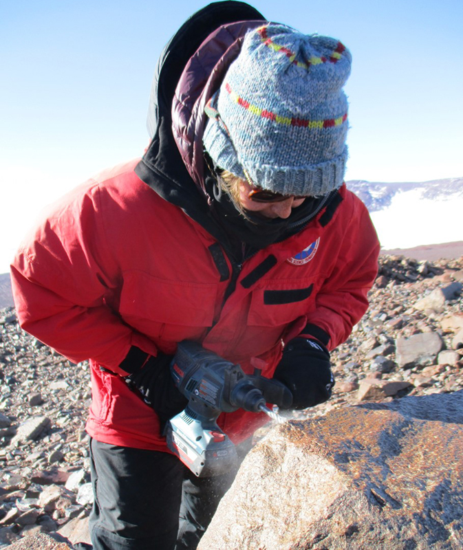 Allie Belter drills into a large stone on the ground to extract a sample of it